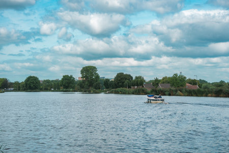 Boat traveling across a lake in Holland, with vegetation in the background on a warm day in the Netherlands.の写真素材