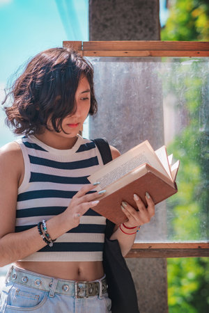 Young woman, take a book from a box of books on the street, she is standing on the sidewalk, these boxes of books are typical in European countries that encourage reading among their inhabitants.の写真素材