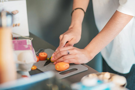 Close-up of a young woman's hands cutting vegetables on a cutting board in her kitchen, food concept.の写真素材