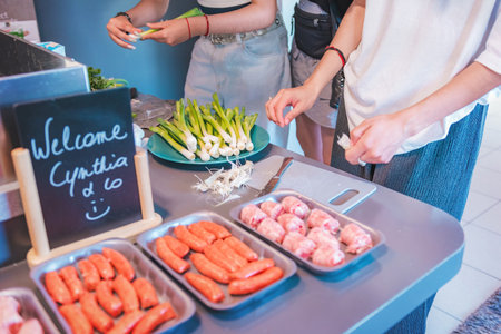 Cold meats and sausages arranged on plates, and two women whose hands can be seen arranging and cutting chives, are in the kitchen.の写真素材
