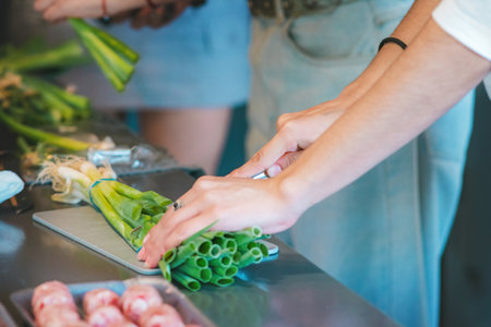 Cold meats and sausages arranged on plates, and two women whose hands can be seen arranging and cutting chives, are in the kitchen of their home.の写真素材