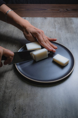 At home, you can see a woman's hands cutting organic soap paste to make natural bath soaps....
