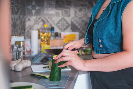 In her kitchen, a woman cuts a zucchini with a kitchen knife. Preparation of homemade food.の写真素材