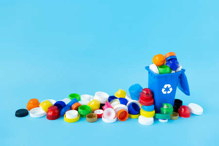 Miniature recycling container filled with plastic bottle caps of different sizes, shapes and colors...