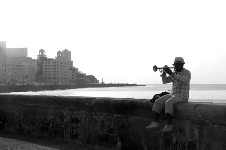 HAVANA, CUBA - APRIL 1, 2017: Black male Cuban street musician with hat and sunglasses playing the trumpet sitting on the Malecon in Havanaのeditorial素材