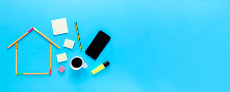 Top view of fluorescent marker pens forming a drawing of a house, other stationery materials, a cup of coffee and smartphone on pastel blue background, space for text. Workspace concept.の写真素材