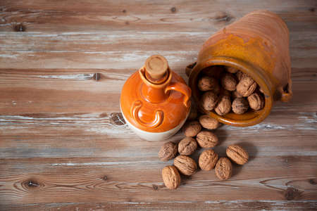 Clay vessel with nuts scattered on aged wooden board. Space for text. Healthy food concept.の写真素材