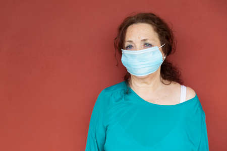Portrait of old woman with protective face mask on red wall. Confinement by coronavirus. Covid-19 concept.の写真素材