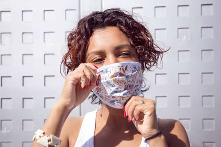 Close-up of brown-skinned girl adjusting her face mask on the street. Concept of new normality and social distancing.の写真素材