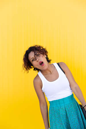 Young woman with brown skin smiling as she shows a shopping bag on a yellow wall. Space for text....