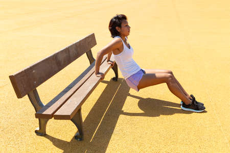 Young woman exercising her body with the help of a bench. She's in an outdoor park. Space for text.の写真素材