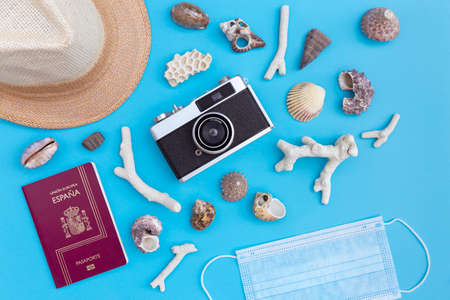 Top view of straw hat, protective face mask, passport, analog photo camera and beach shells on blue background. Coronavirus covid-19, summer vacation and travel concept.の写真素材