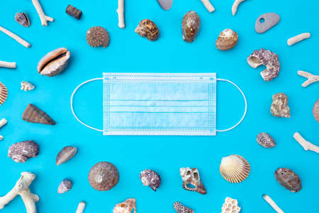 Top view of medical face mask and seashells on a blue background. Coronavirus covid-19, summer...