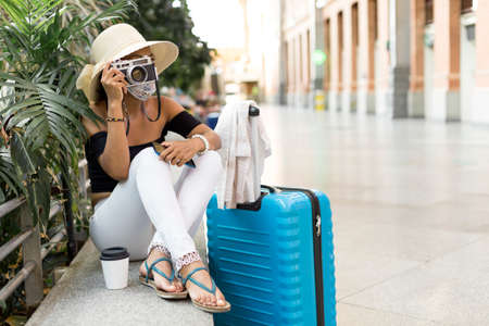 Traveling woman taking a photograph with an analogue camera inside a transport station. Space for text. Summer, holiday and travel concept.の写真素材