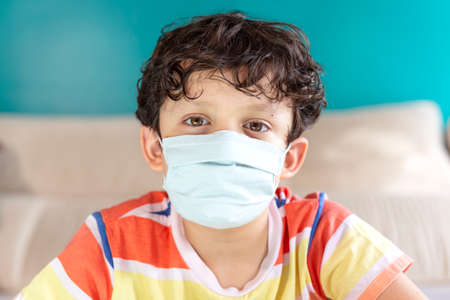 Portrait of little boy at home wearing a face mask. Virus protection and infection control concepts.の写真素材