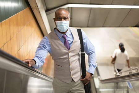 Black man with medical mask climbing subway stairs. Concept of social distancing in context of...
