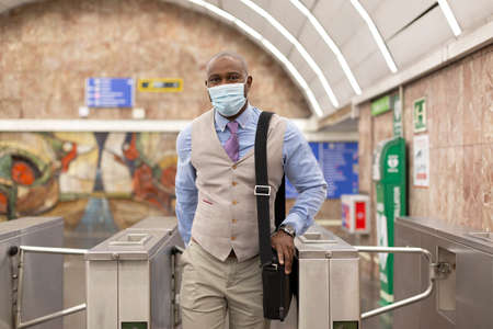 Elegant black man walking out of a subway station. He is wearing a face mask. Concept of return to work after confinement.の写真素材