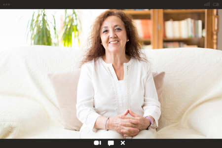 View of a personal computer screen with a portrait of a smiling woman during a video call. She is at...