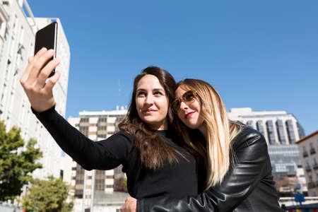 Two girls hugging and taking a selfie in the city.