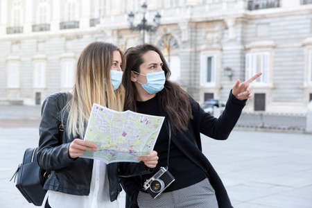 Two girls traveling together in the city. They have a tourist map and are wearing medical masks....