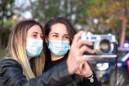Close up of two girls wearing face masks with an analog camera in their hands.の写真素材
