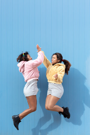 Two friendly girls jumping and clapping their hands in the air on a blue background. Space for text. Friendship concept.の写真素材
