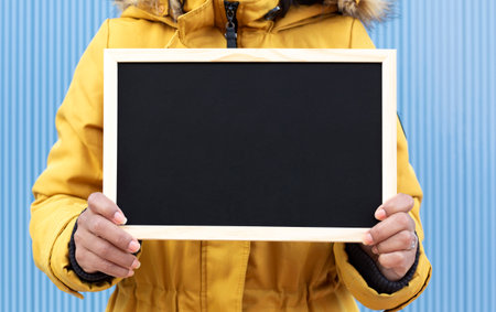 Close up of unrecognizable person holding a blank chalkboard. Blue background. Space for text.