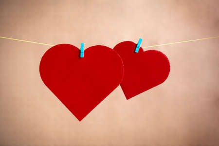 Two hearts made of cardboard and painted in red lying on a rope with clamps. Valentine's Day...