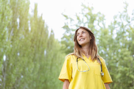 Portrait of smiling young female nurse with stethoscope looking at the sky. She is outdoors nature. Space for text.の写真素材