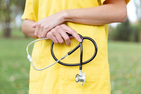 Close up of a nurse's hands holding a stethoscope. She is outdoors.の写真素材