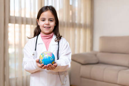 Little girl dressed as a doctor holding a world ball in her hands. World Health Day concept. Space for text.の写真素材