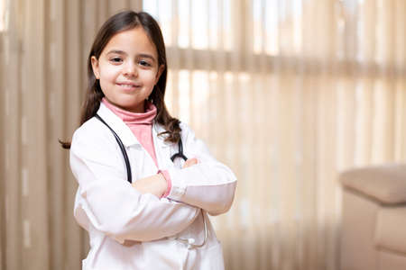 Portrait of little girl in doctor's uniform posing smiling with arms crossed. Concept of health and wellness. Space for text.の写真素材