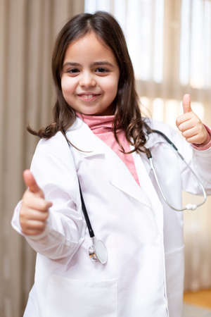 Portrait of smiling little girl dressed as a doctor giving thumbs up.の写真素材