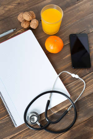 Top view of a doctor's work desk. Notebook, stethoscope and mobile phone on dark wood background.の写真素材