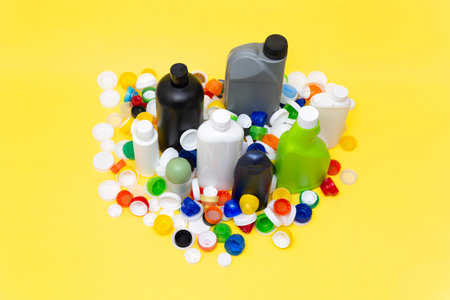 Various plastic containers of different sizes and shapes and many caps isolated on yellow...