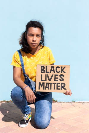 Portrait of Latin American woman with serious attitude holding a banner with slogan Black Lives...