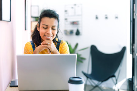Young latina woman using a laptop at her workplace. Space for text.
