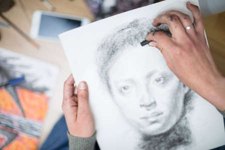 Top view of a close up of the hands of a person drawing a portrait in charcoal on a canvas. Concept of painting classes. Selective focus. Space for text.の写真素材