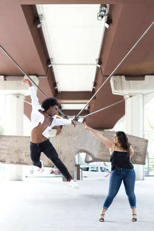 Multiracial couple of dancers doing an acrobatic jump in the city. Street dance concept. Space for...