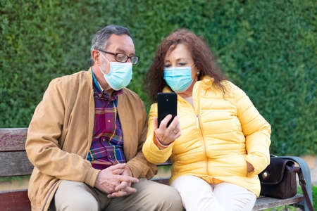 Caucasian elderly couple using a mobile phone. They are outdoors and wearing face masks.