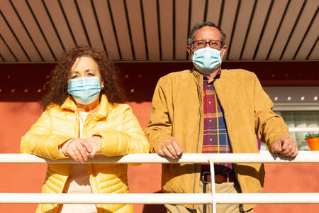 Portrait of two senior citizens observing the outside from the porch of their home. They are wearing...