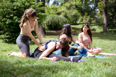 Yoga class in the park. Instructor helping one of the girls while the rest are resting. Concept of health and wellness.の写真素材