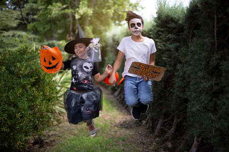 Caucasian boy and girl in typical Halloween costumes jumping and having fun outdoors.の写真素材