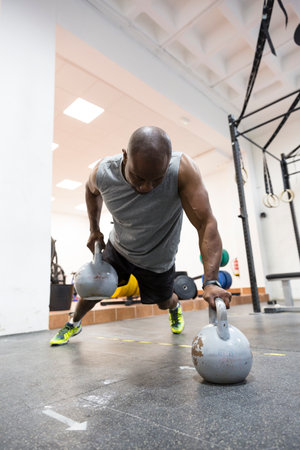 Black muscular man doing physical training with kettlebells in gym.の写真素材