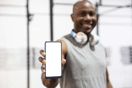 Black sportsman smiling showing the blank screen of a smartphone. Concept of sports apps. Selective...