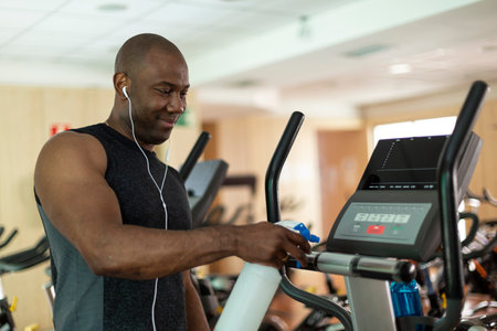Black male athlete cleaning a cardio machine with disinfectant at the gym. Selective focus.の写真素材