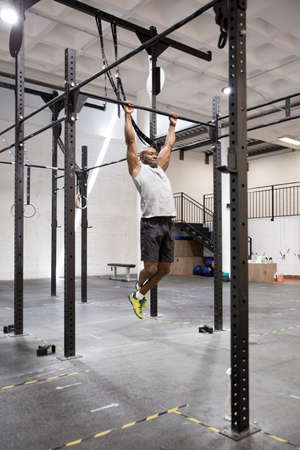 Young black man doing fitness workout on fixed bar in gym.