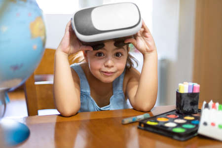 Funny little Caucasian girl at her desk playing with a pair of virtual reality glasses.の写真素材