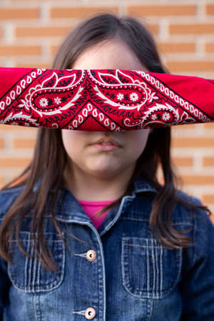 Close up of the face of a little girl with her eyes covered by a handkerchief. Face without identity, unrecognizable person.の写真素材