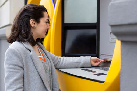 Elegant woman withdrawing cash at an ATM machine. Space for text.の写真素材